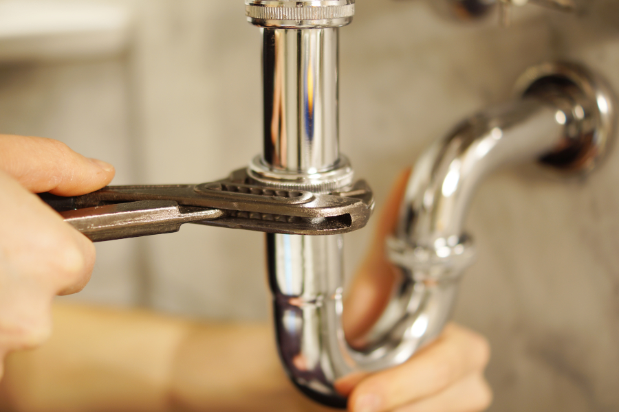 Plumbing repair service. Professional installer with spanner checking pipe.